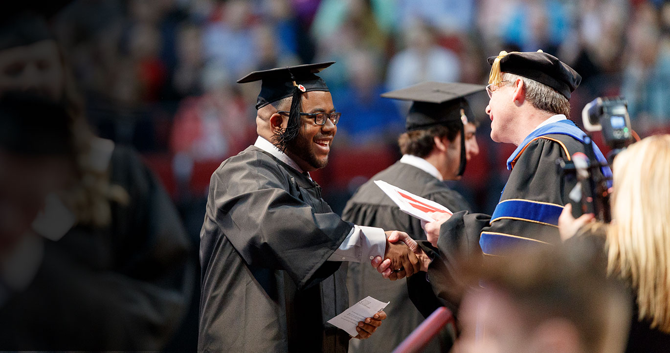 smiling graduating student shakes professors hand after receiving his diploma