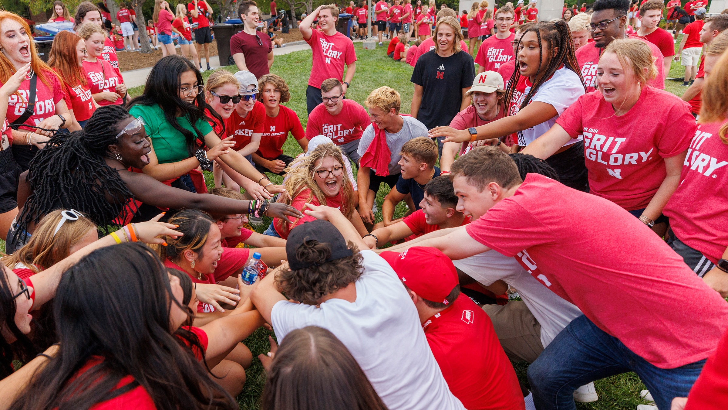 A group of students standing outside putting their hands in a circle in a celebratory manner